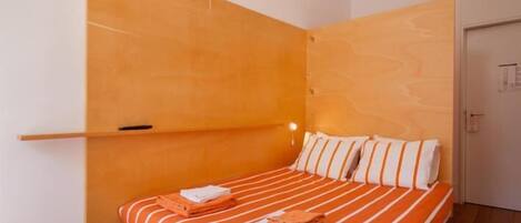 A bedroom with a bed, orange and white striped bedding, a wooden headboard, and a red rug.