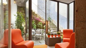 A modern interior with orange chairs, a glass wall, and a view of a staircase and outdoor seating area. - Porto Lounge Hostel & Guesthouse (Porto)
