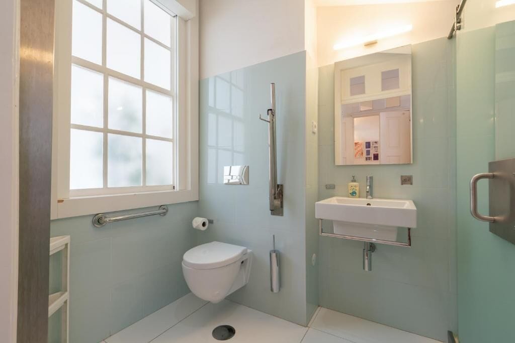 A bathroom with a toilet, a sink, a mirror, and a window.