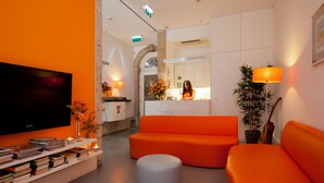 A modern lobby with orange sofas, a flat-screen TV, books, and a reception desk. - Porto Lounge Hostel & Guesthouse (Porto)