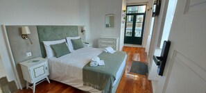 Quarto com cama, mesas de cabeceira, um espelho e porta que dá para uma varanda.