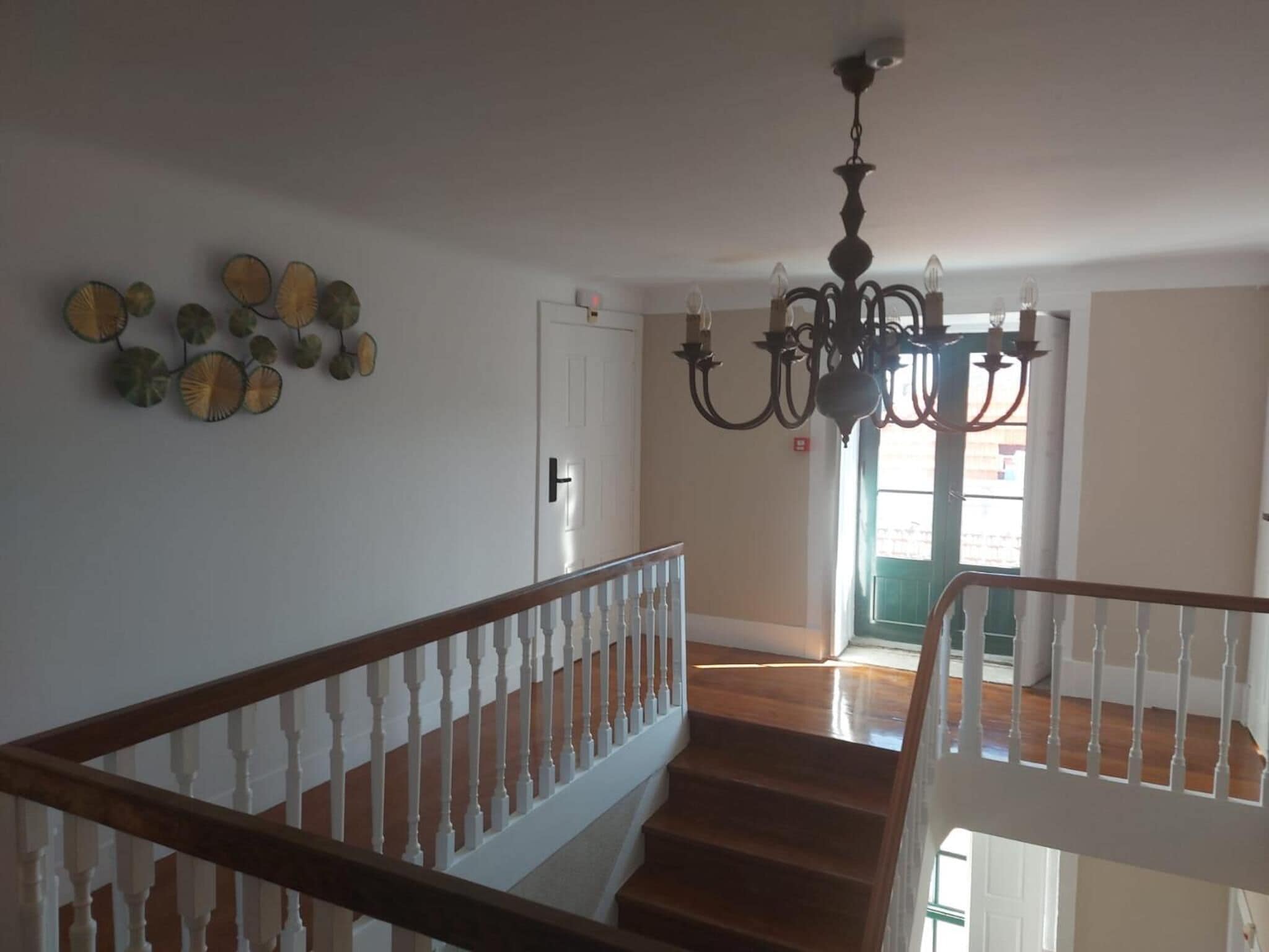 A staircase with white balusters and wooden handrails, leading to a room with a chandelier and a door with a light switch.