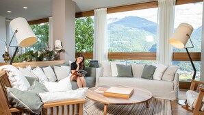 A modern living room with a sofa, two lamps, a coffee table, and a view of mountains through large windows.