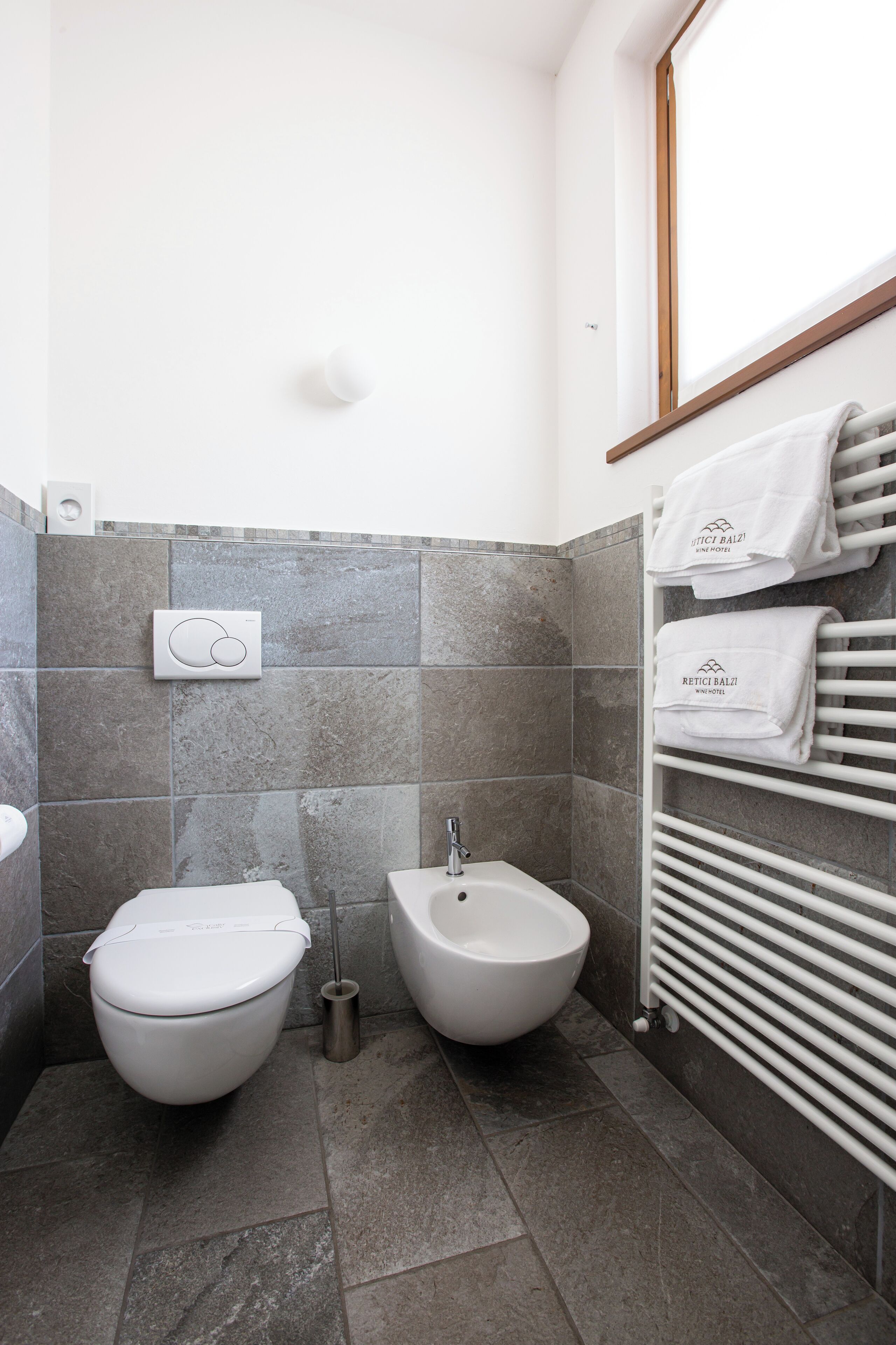 Een moderne badkamer met toilet, bidet en een handdoekrek met handdoeken.