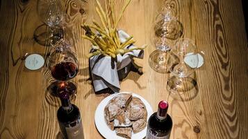 Una mesa de madera con copas de vino, una botella de vino, un plato de pan y una cesta de papas fritas.