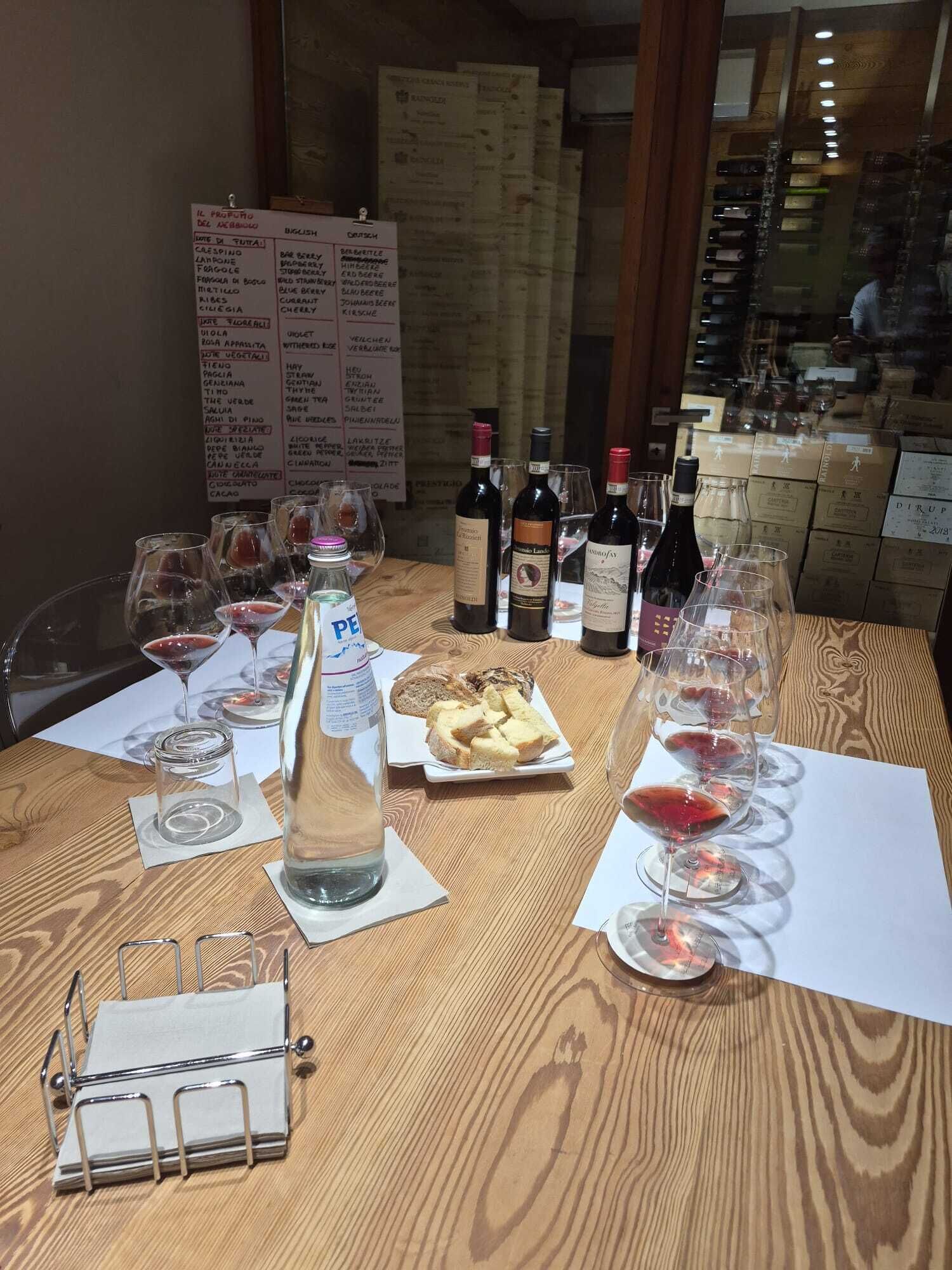 A wooden table with wine glasses, bottles, and a menu board in the background.
