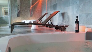 A spa area with a hot tub, lounge chairs, a bottle of wine, and candles.