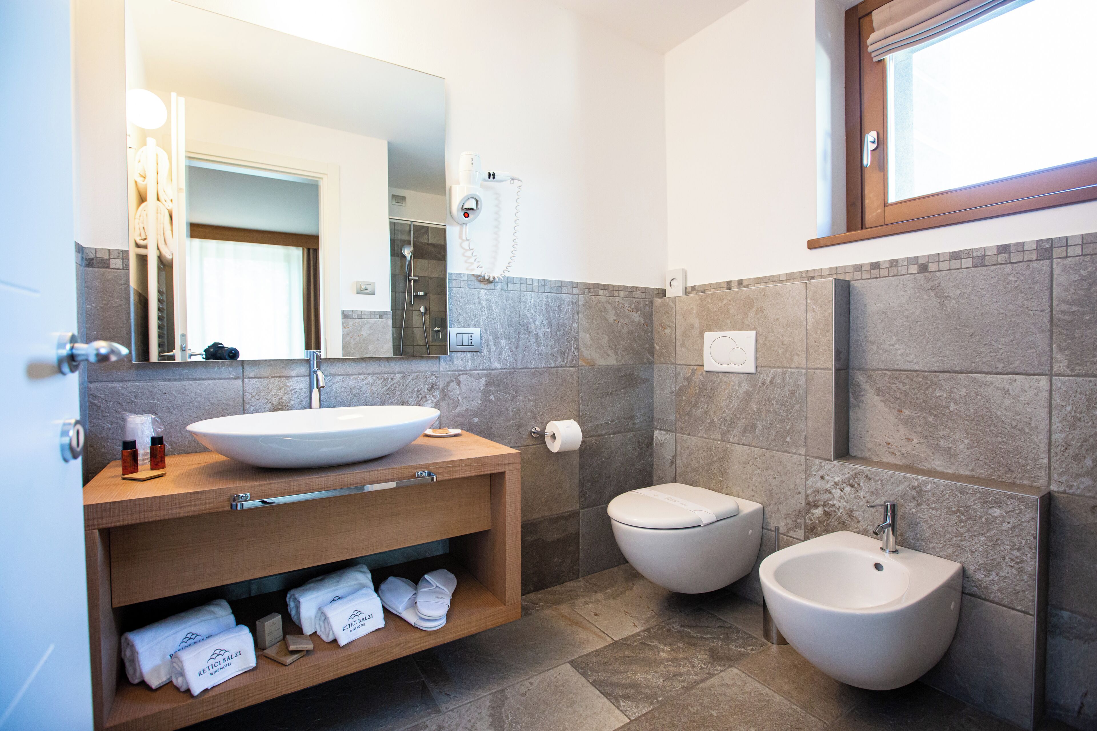 A modern bathroom with a large mirror, a sink, a bidet, and a vanity with towels.