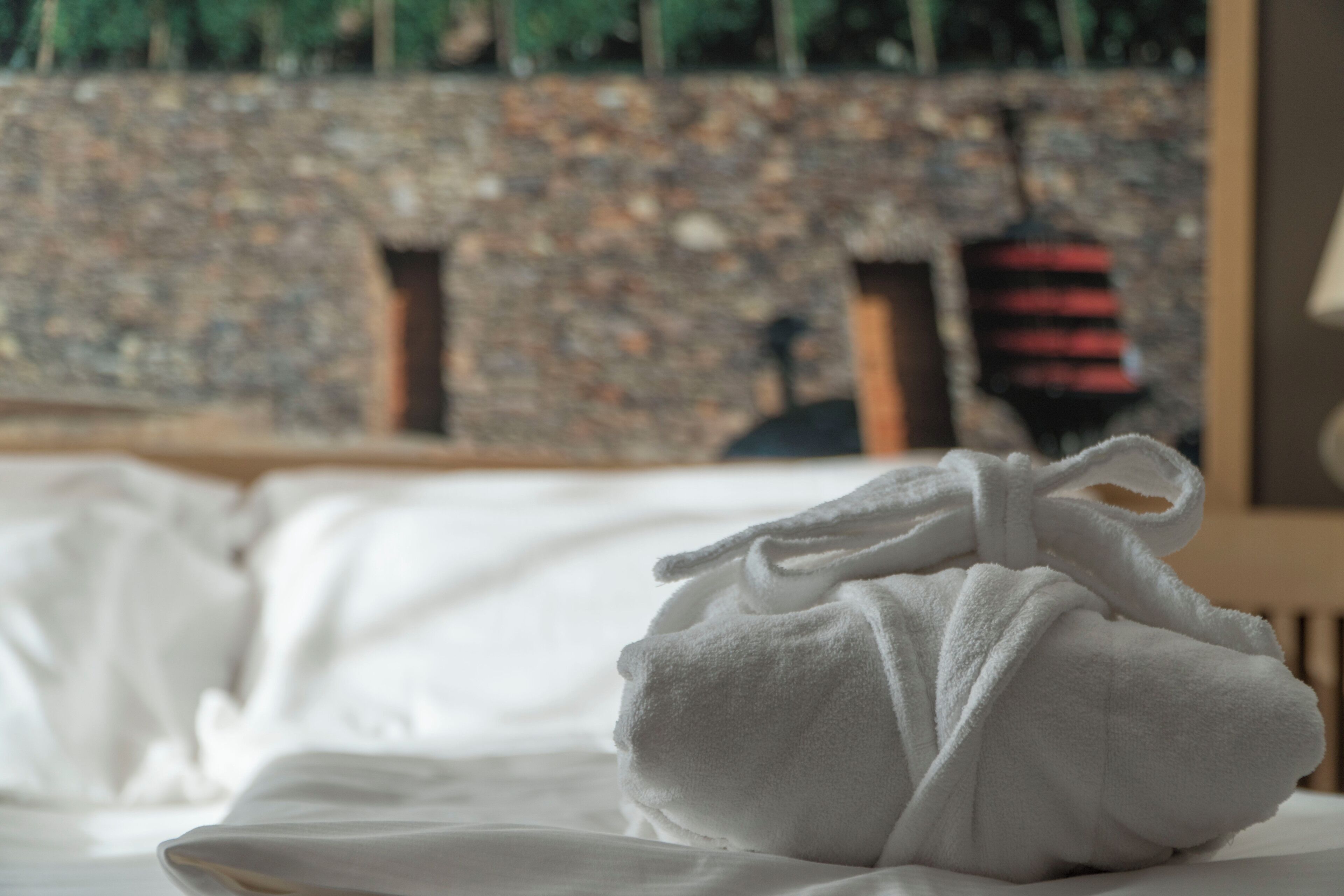 Ein ordentlich gemachtes Bett mit einem weißen Handtuch darauf, eine Steinsäule im Hintergrund und ein Holzstuhl.