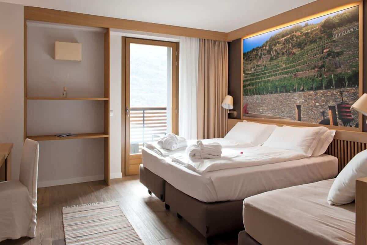 A hotel room with a bed, a desk, and a large window with a view of a vineyard.