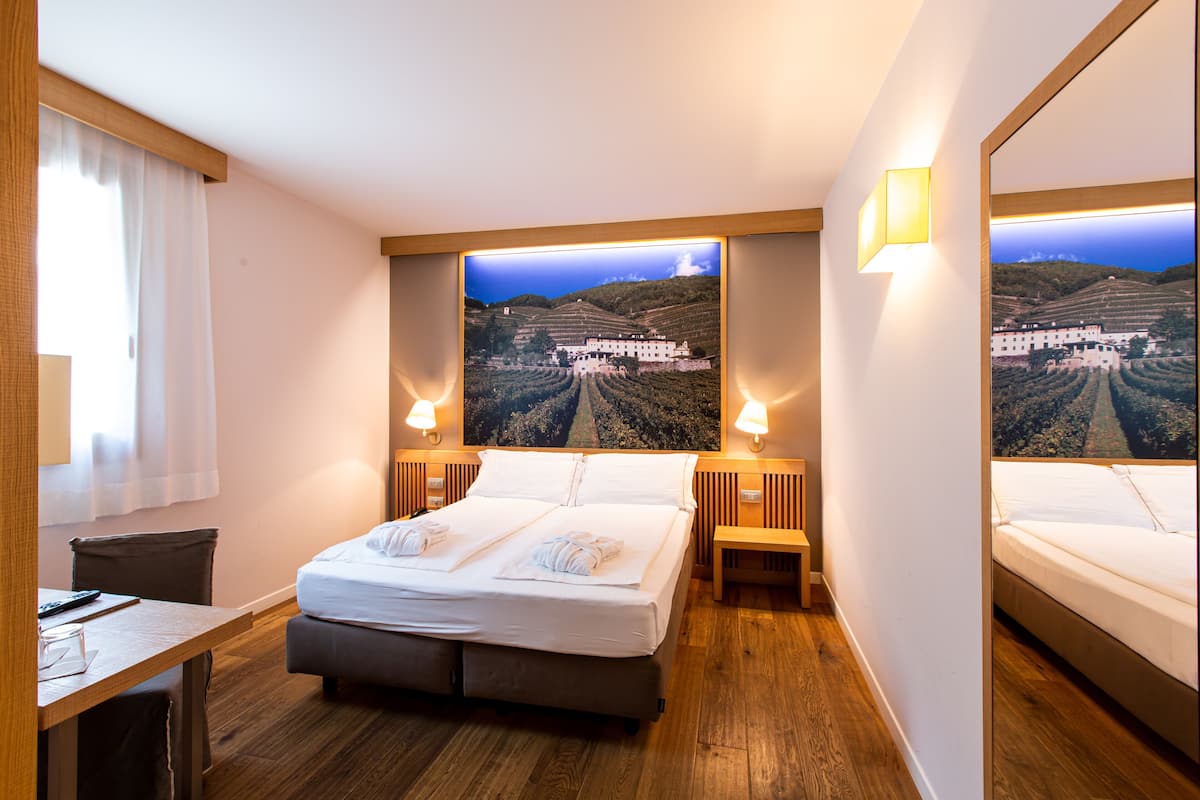 A hotel room with a large bed, two bedside tables, a desk, and a mirror.