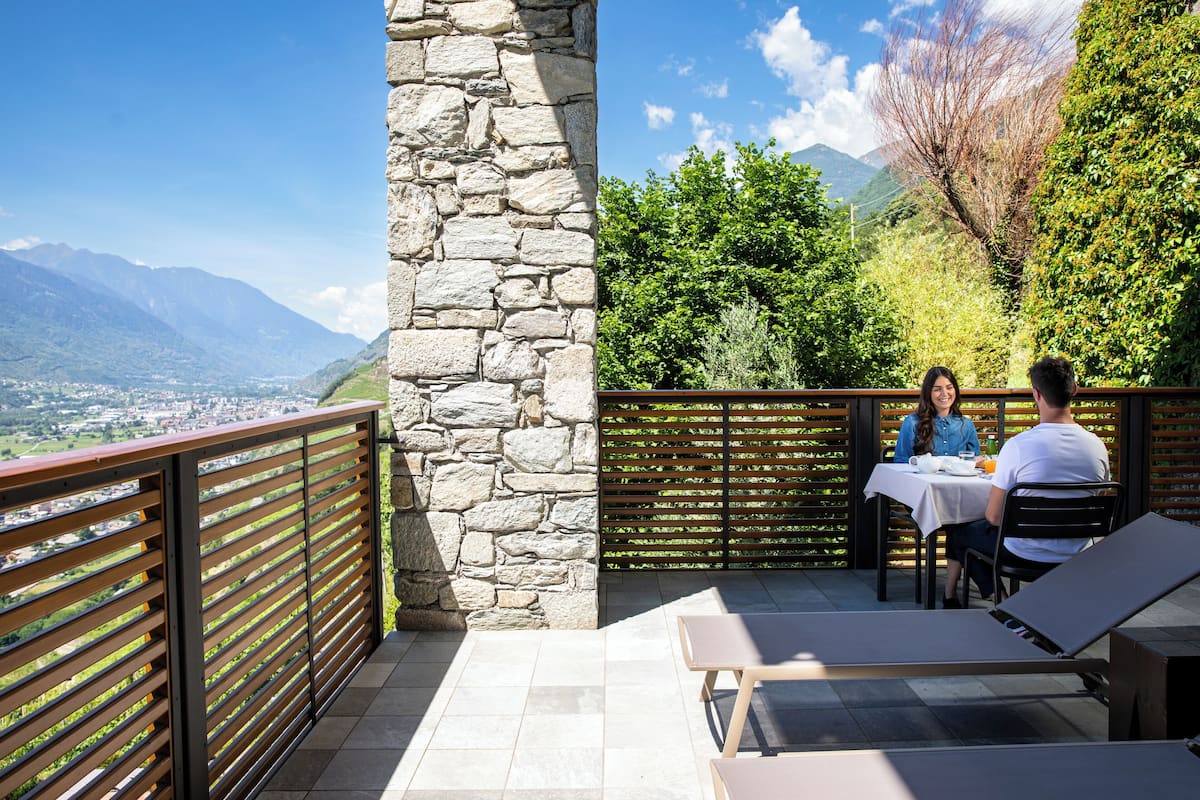 A terrace with stone walls, a wooden railing, and a table with two people dining.