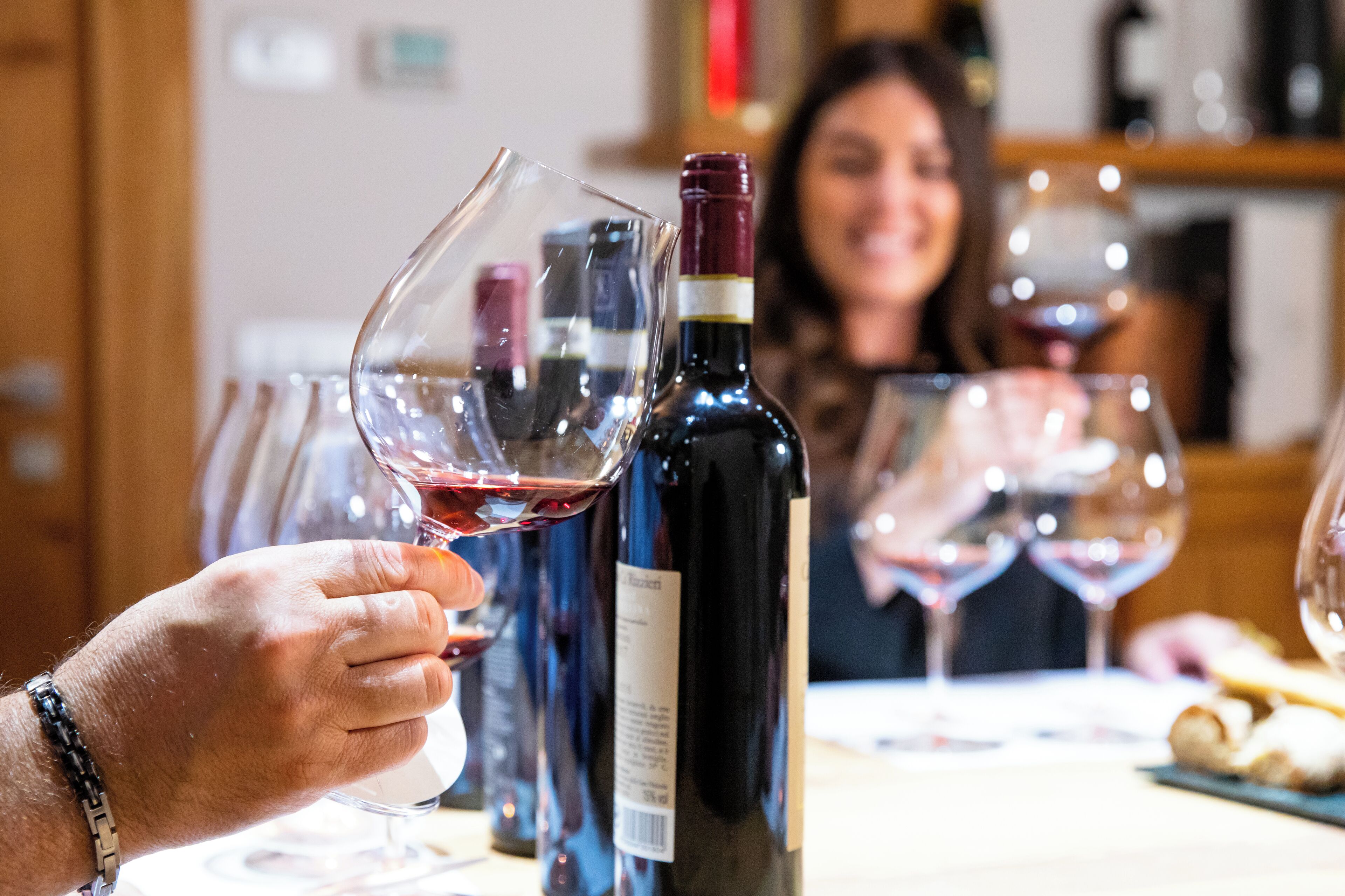 Una persona sosteniendo una copa de vino, con una botella de vino al fondo.