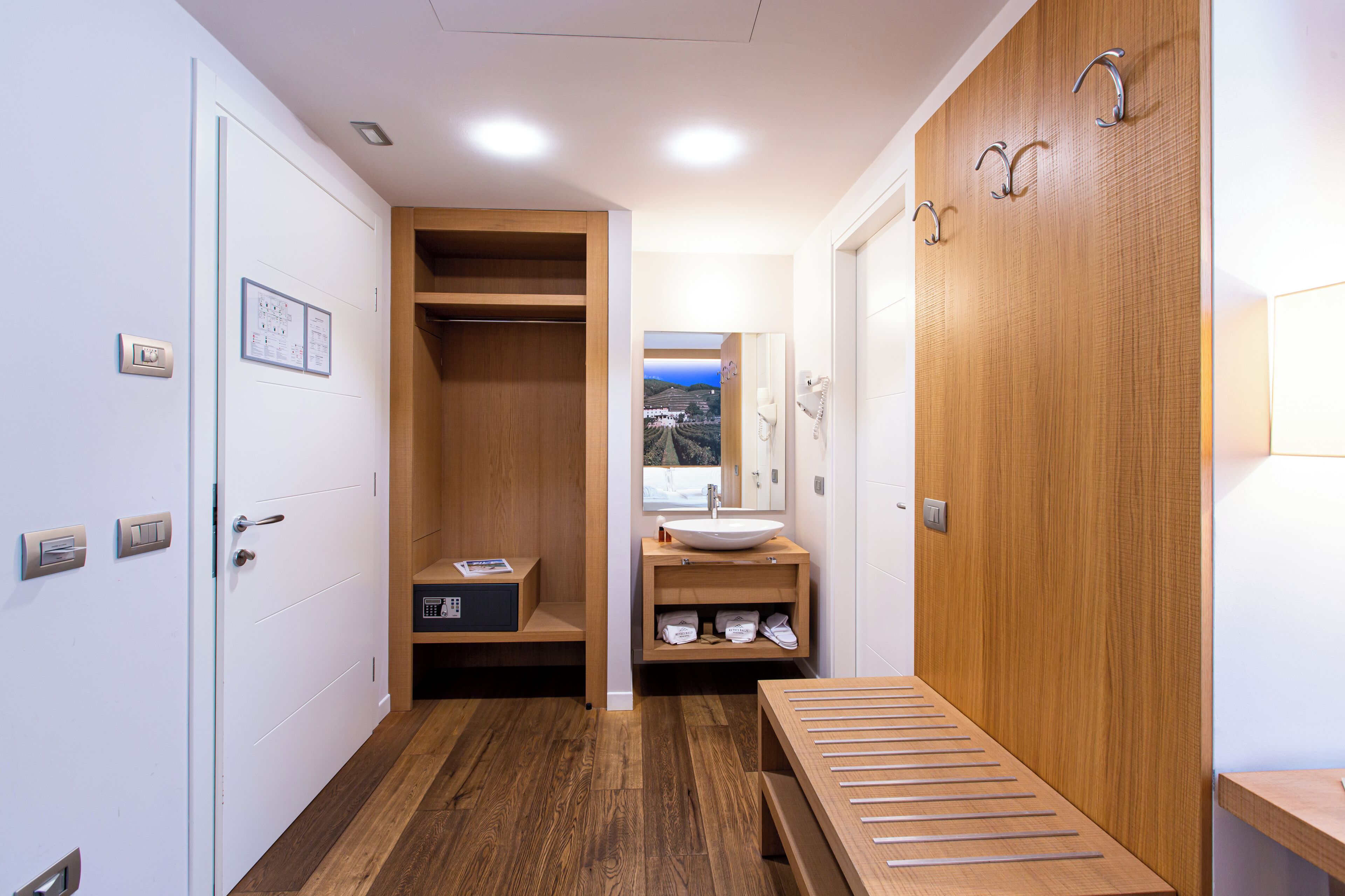 Un baño moderno con un mueble tocador de madera, un lavabo y un espejo. Hay un banco de madera y un perchero para toallas.