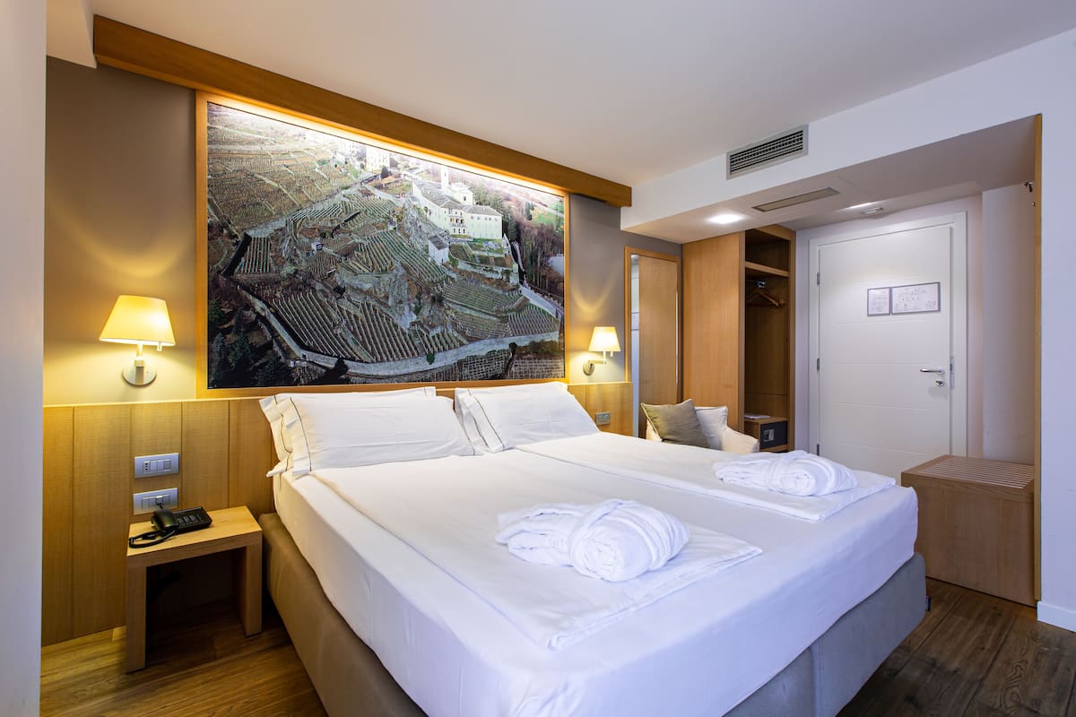 A hotel room with a large bed, two bedside lamps, a nightstand with a phone, a wooden headboard, and a large framed picture on the wall.