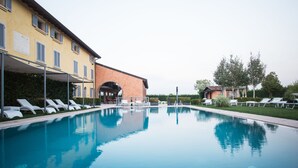 A swimming pool with lounge chairs and a building with multiple windows and a covered area. - Hotel Corte del Paggio (Valeggio sul Mincio)