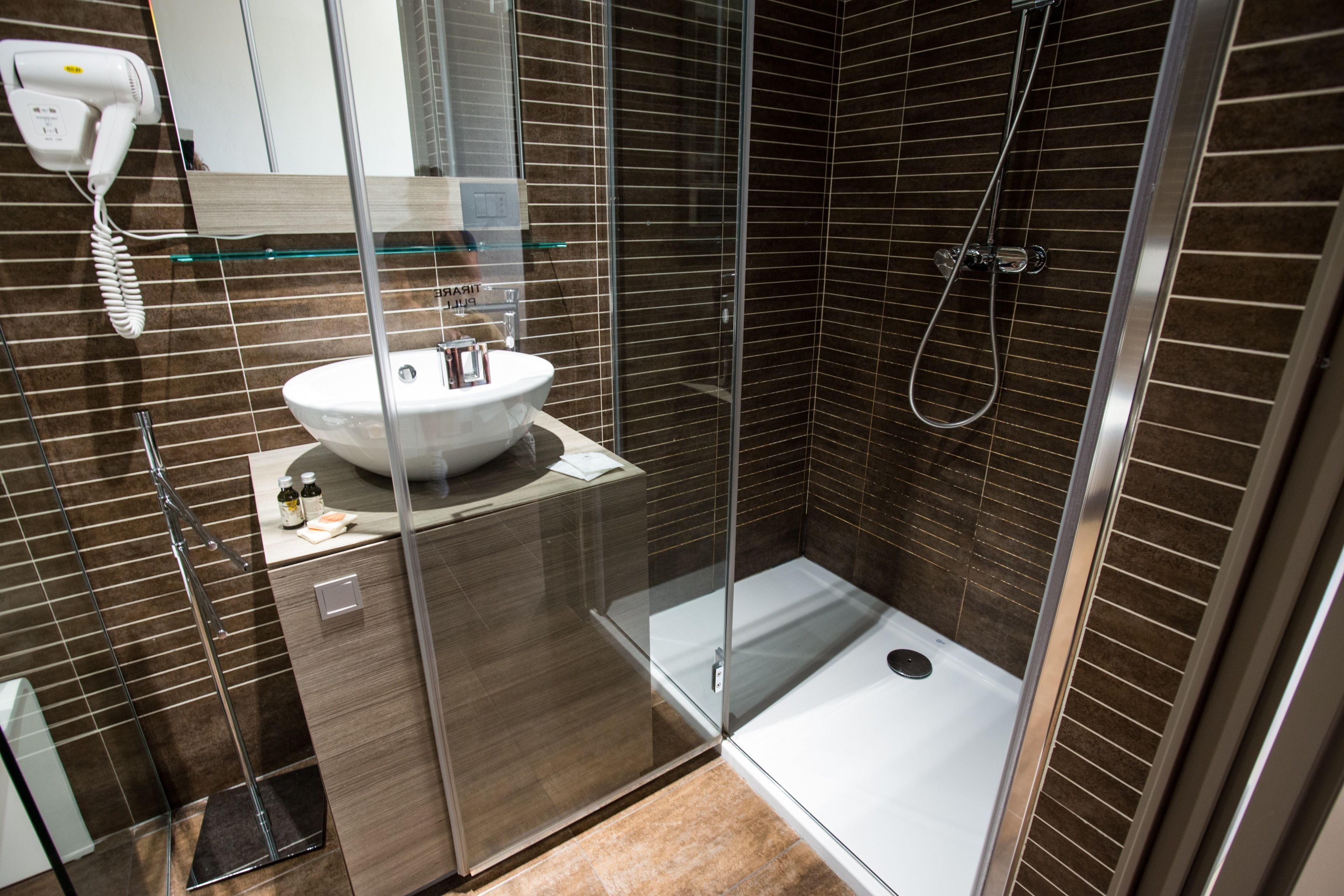 Ein modernes Badezimmer mit einer gläsernen Duschkabine, einem weißen Waschbecken und einem an der Wand montierten Föhn.