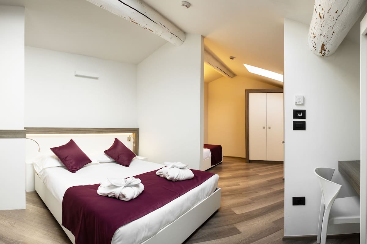 A modern hotel room with a large bed, a desk, and a wardrobe.
