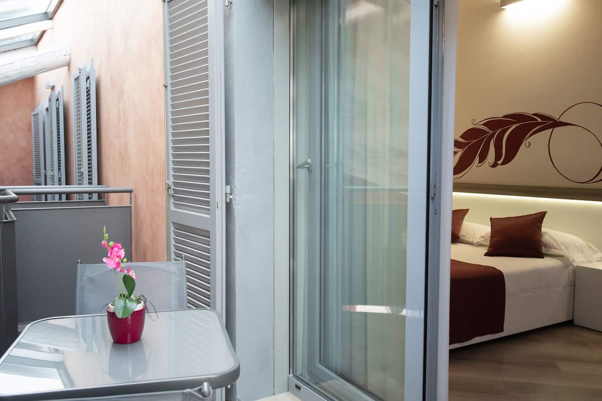 A modern hotel room with a glass door leading to a balcony, a bed with white and brown bedding, and a decorative wall art piece.