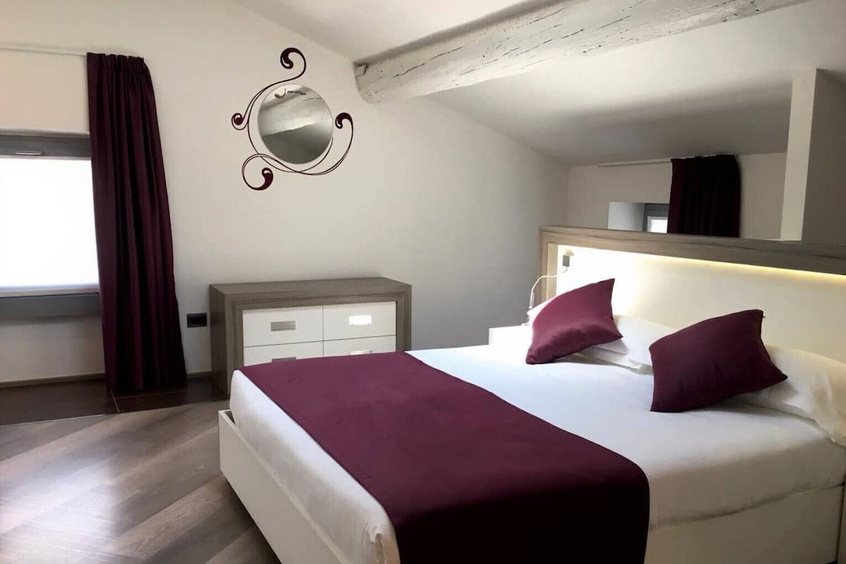 A bedroom with a bed, a bedside table, a mirror, and a window with curtains.