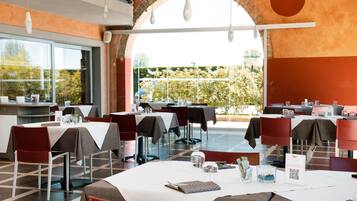 Un ristorante con tavoli apparecchiati, un arco in mattoni e vista sul verde.