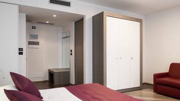 Une chambre d’hôtel moderne avec un lit, un canapé rouge, une armoire et une salle de bain visible à travers une porte ouverte.