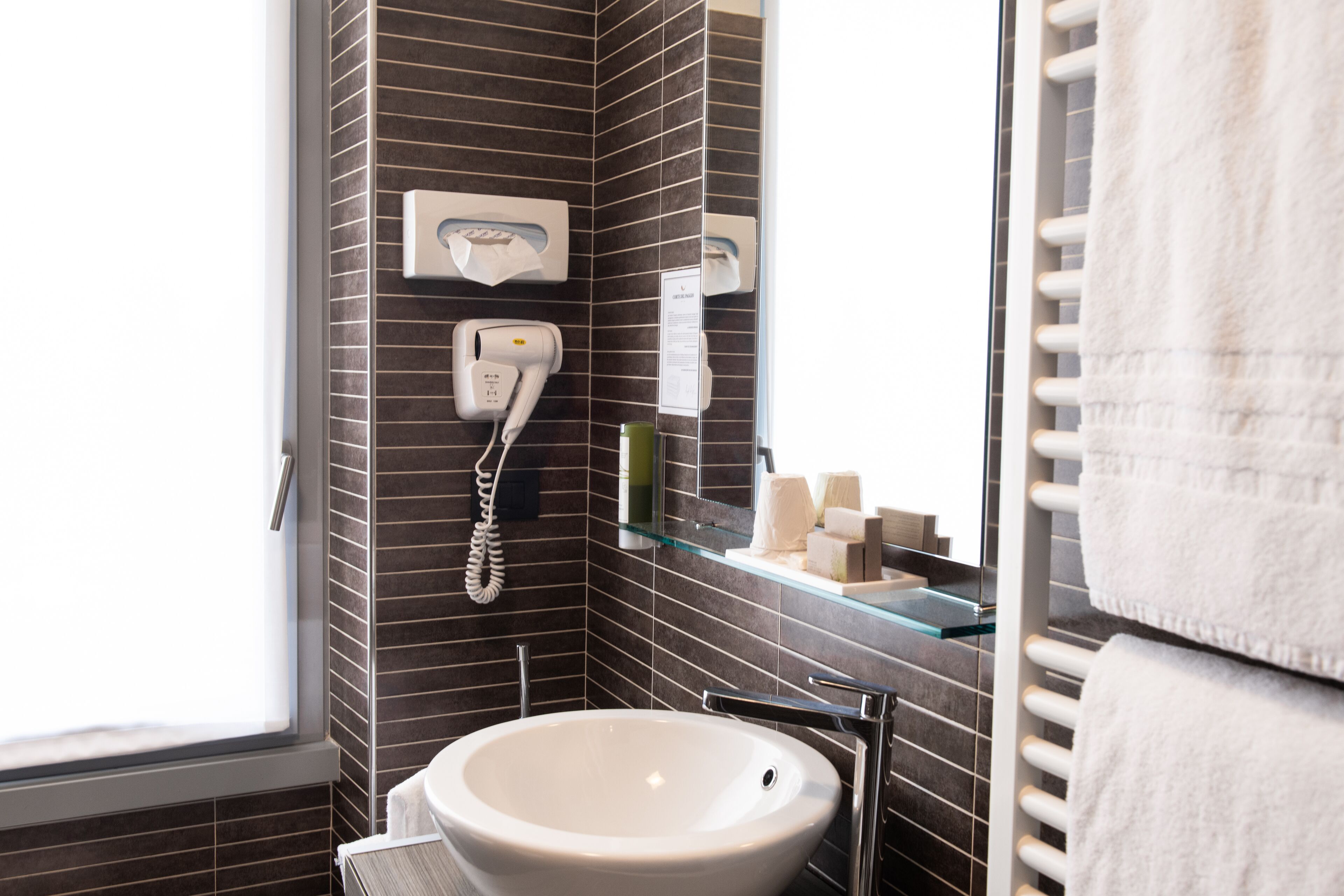 Ein Badezimmer mit einem weißen Waschbecken, einem Handtuchhalter, einer Glasablage für Pflegeprodukte und einem Spiegel.