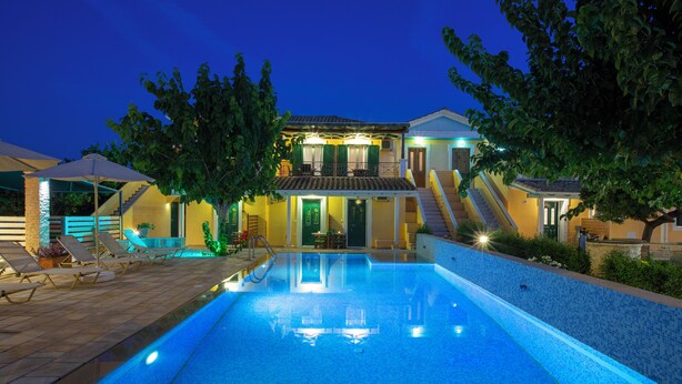 Une piscine avec une terrasse carrelée, un escalier menant à un deuxième étage et un bâtiment doté d’un balcon.