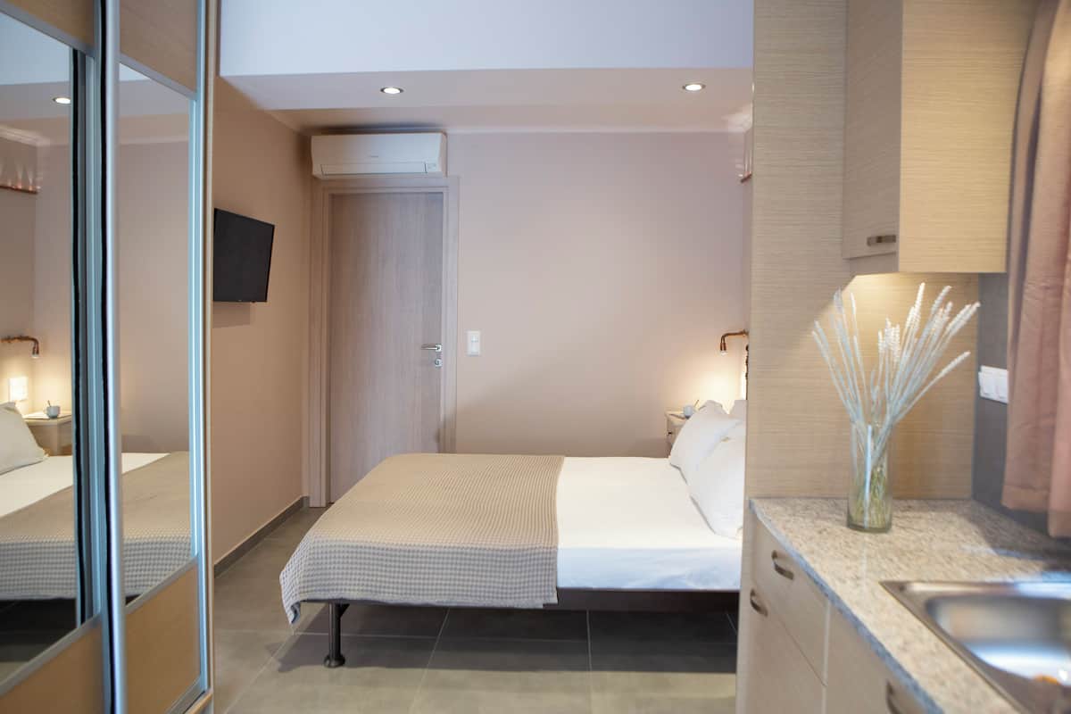 Ein Hotelzimmer mit Bett, Nachttisch, Spiegel und einer kleinen Küchenzeile.
