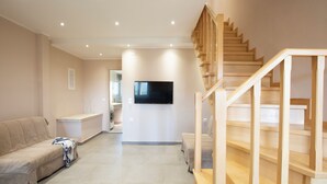 Un salon spacieux avec un escalier en bois, un téléviseur à écran plat fixé au mur et un canapé beige.