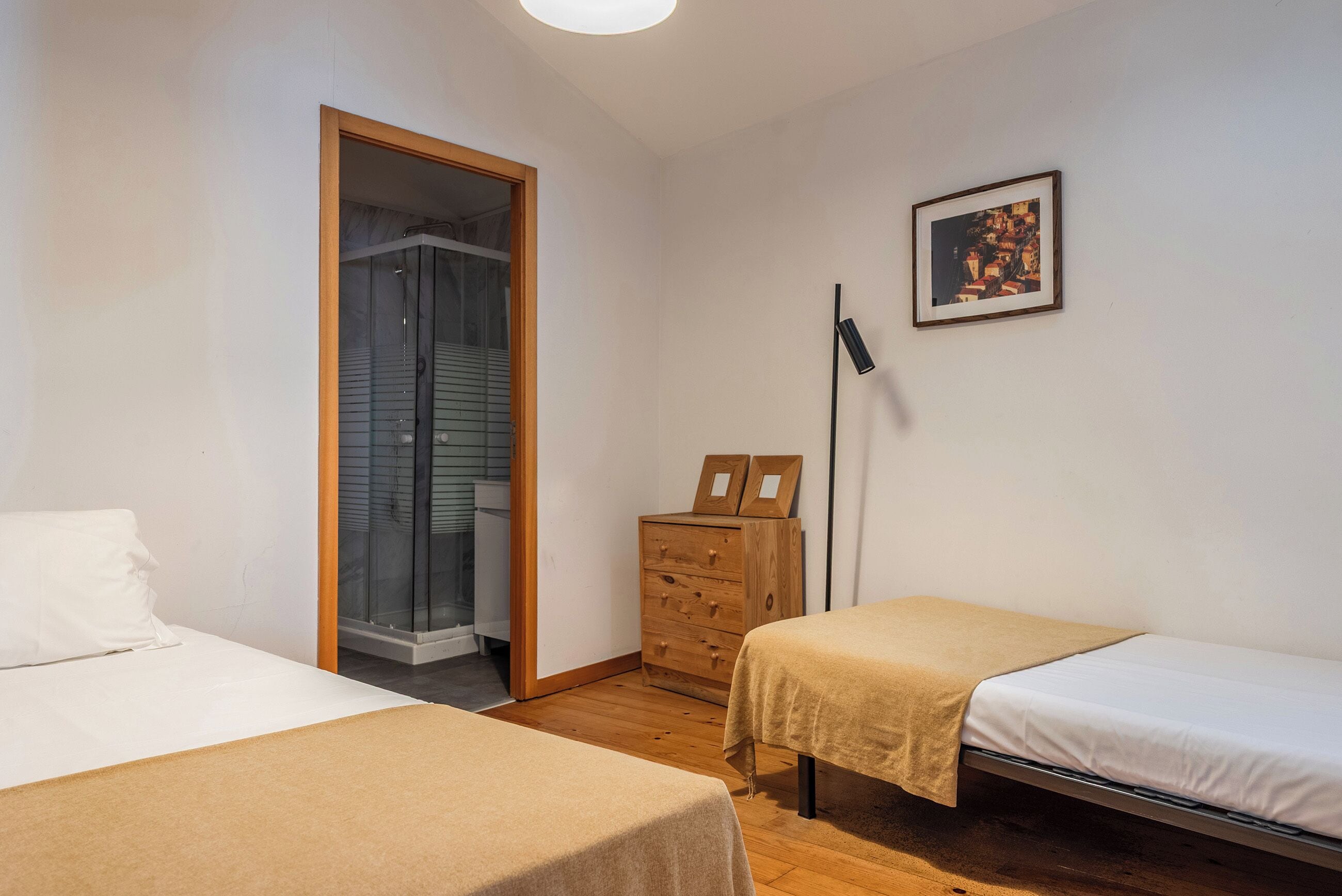 Een slaapkamer met twee bedden, een houten dressoir, een lijst met een foto aan de muur en een deur naar een badkamer.