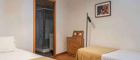 A bedroom with two beds, a wooden dresser, a framed picture on the wall, and a door leading to a bathroom.
