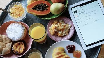 Bandeja de desayuno con diversos alimentos, incluyendo pasteles, un vaso de jugo de naranja y una tableta mostrando un menú.