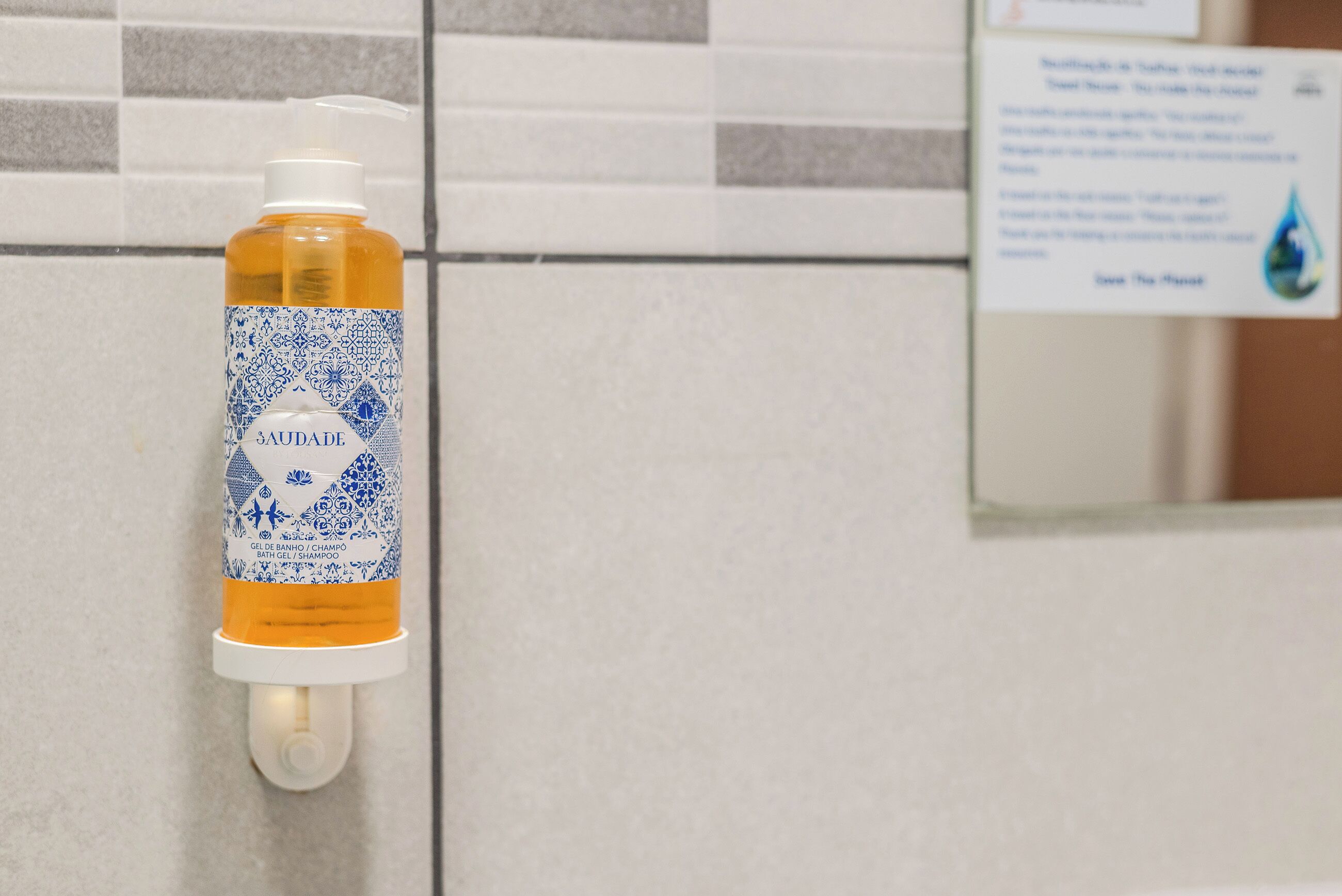 A bathroom with a hand sanitizer dispenser mounted on the wall, a tiled wall, and a sign with water droplet graphics.