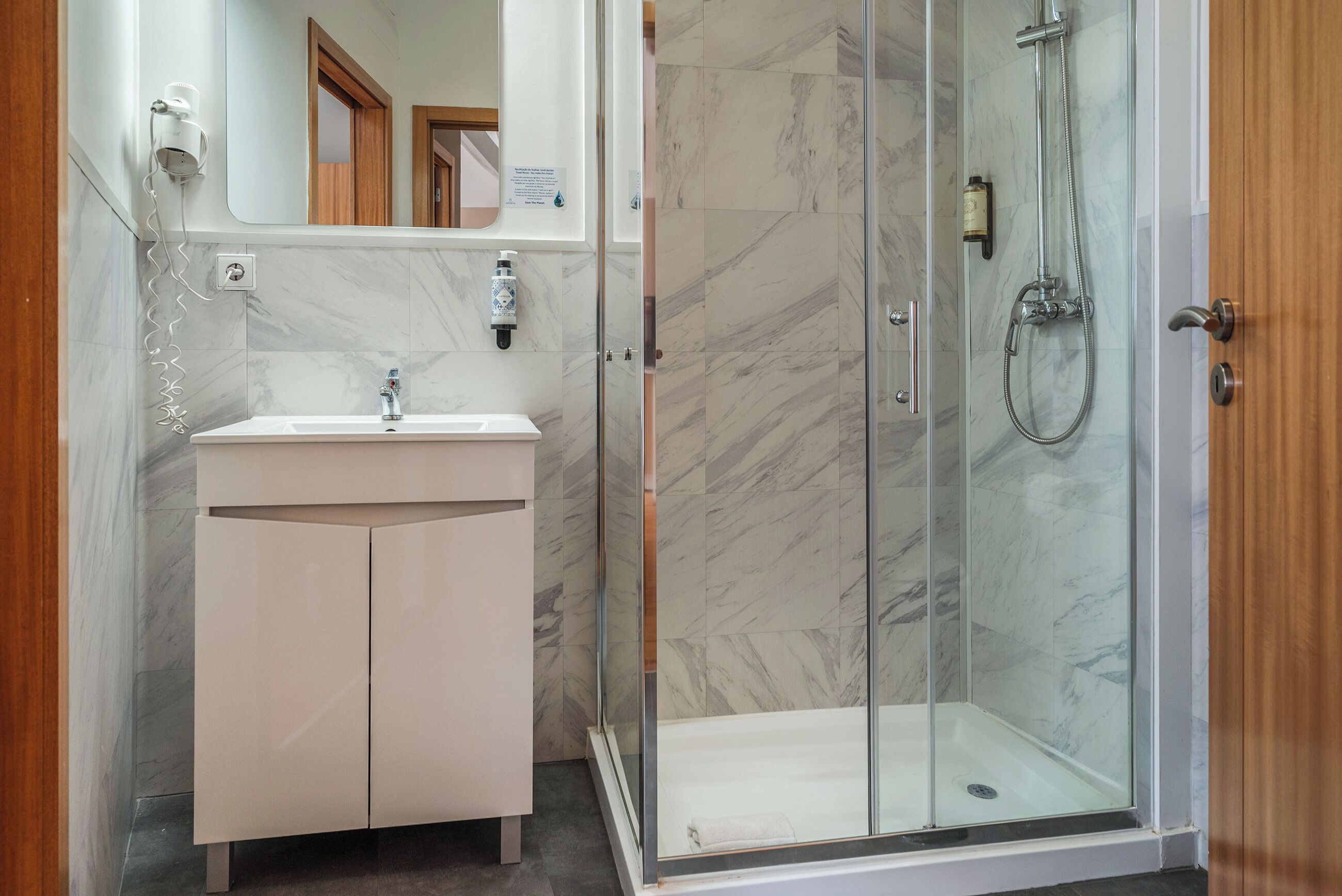 A bathroom with a marble-tiled shower, a white sink, and a mirror.