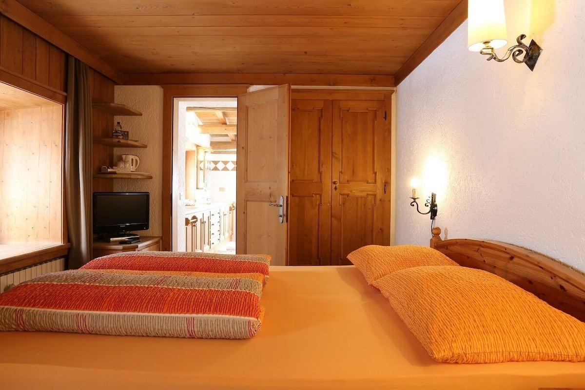 A bedroom with two beds, wooden walls, a television, and a door leading to a kitchen area.
