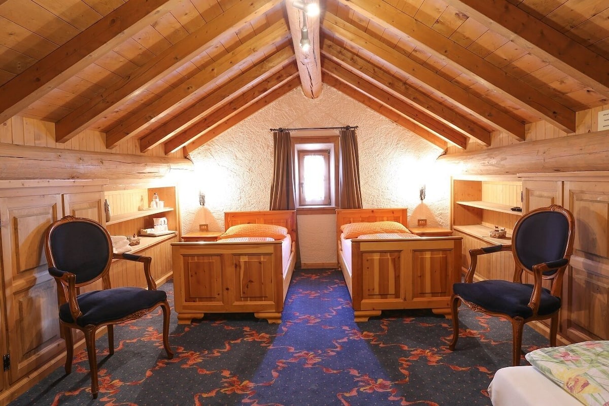 A cozy attic bedroom with two wooden beds, a small window, and a carpeted floor.