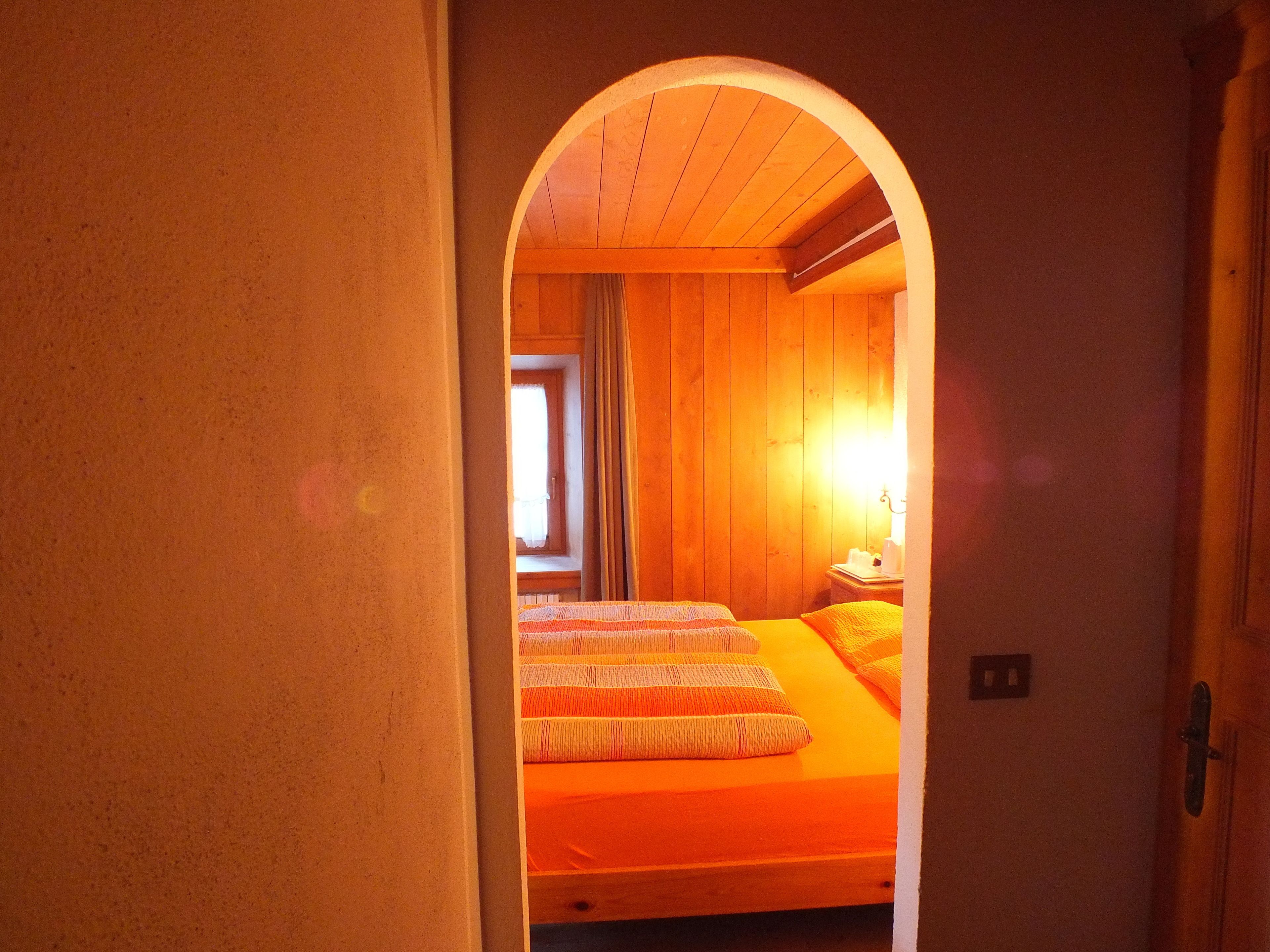 A narrow hallway leading to a room with two beds, wooden walls, and a window with curtains.