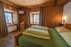 Ett rum med träpanel på väggarna, två sängar, en tv på väggen och ett fönster med gardiner.