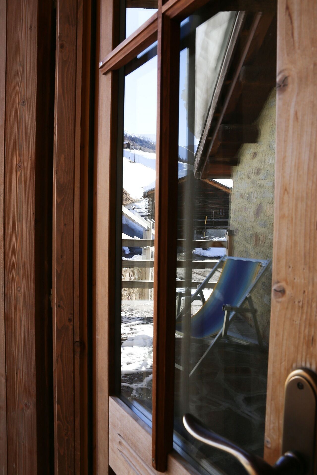 Una ventana con marco de madera que ofrece vistas a un paisaje nevado, que incluye una silla y un edificio.