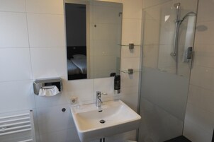 Un baño moderno con un lavamanos blanco, cabina de ducha con mampara de vidrio y un espejo sobre el lavamanos.
