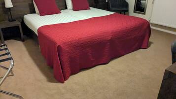 A hotel room with a bed, a chair, a nightstand, a lamp, and a radiator.