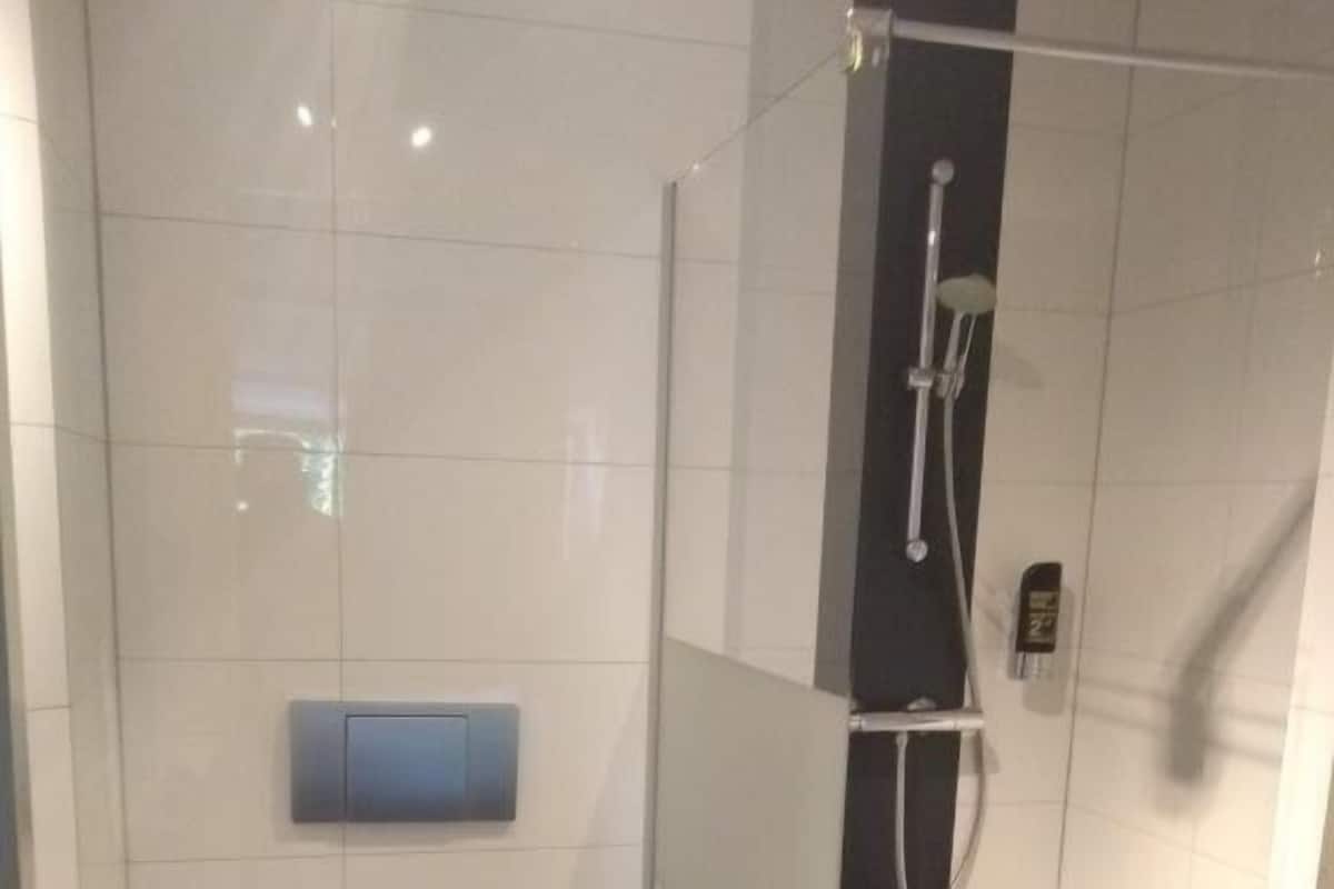 A modern bathroom with a glass-enclosed shower, a toilet, and a hand dryer.