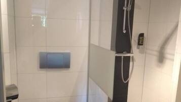 A modern bathroom with a glass-enclosed shower, a toilet, and a hand dryer.