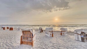 A beach with numbered beach huts and a sunset in the background.