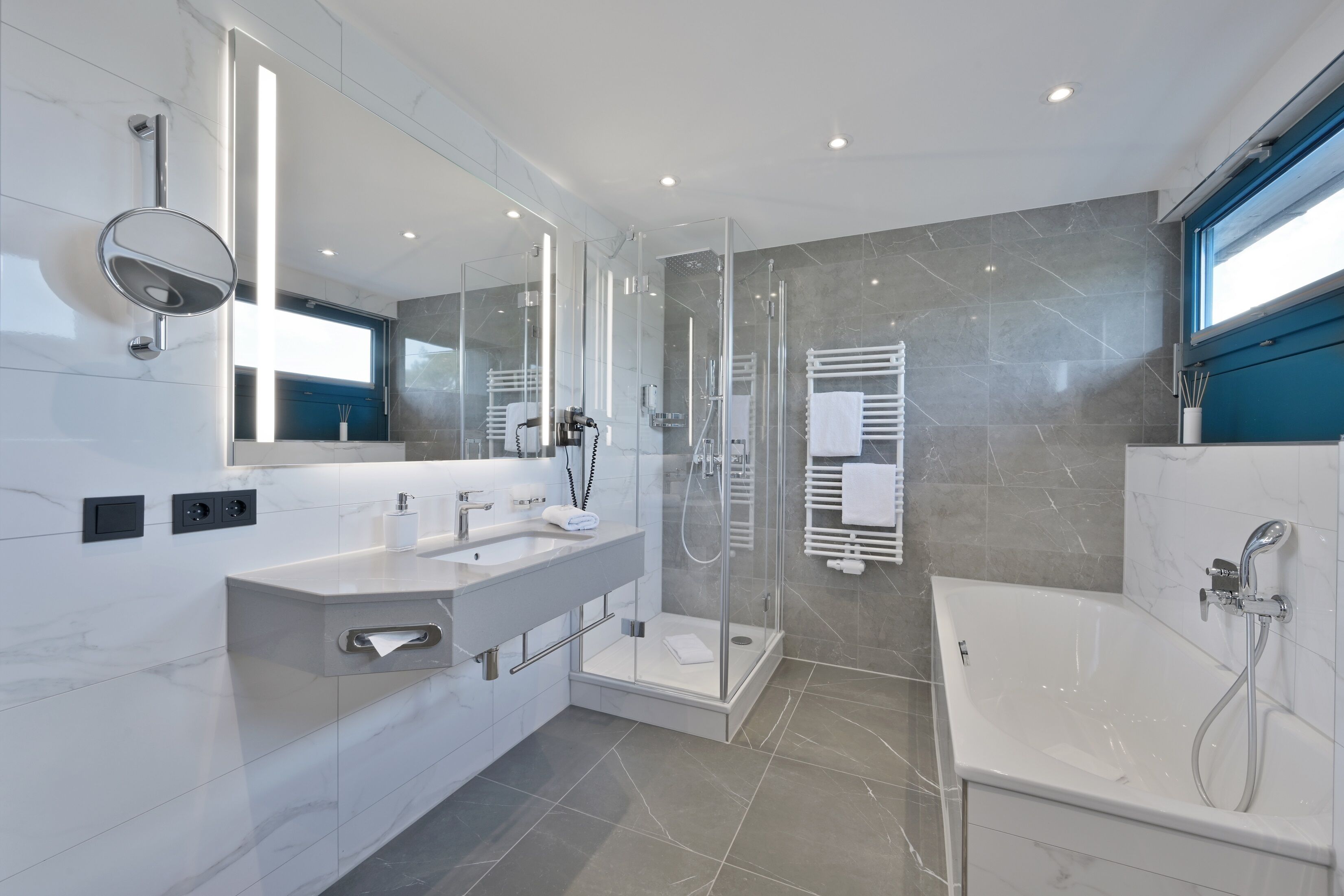 A modern bathroom with a glass-enclosed shower, a large mirror, and a bathtub.