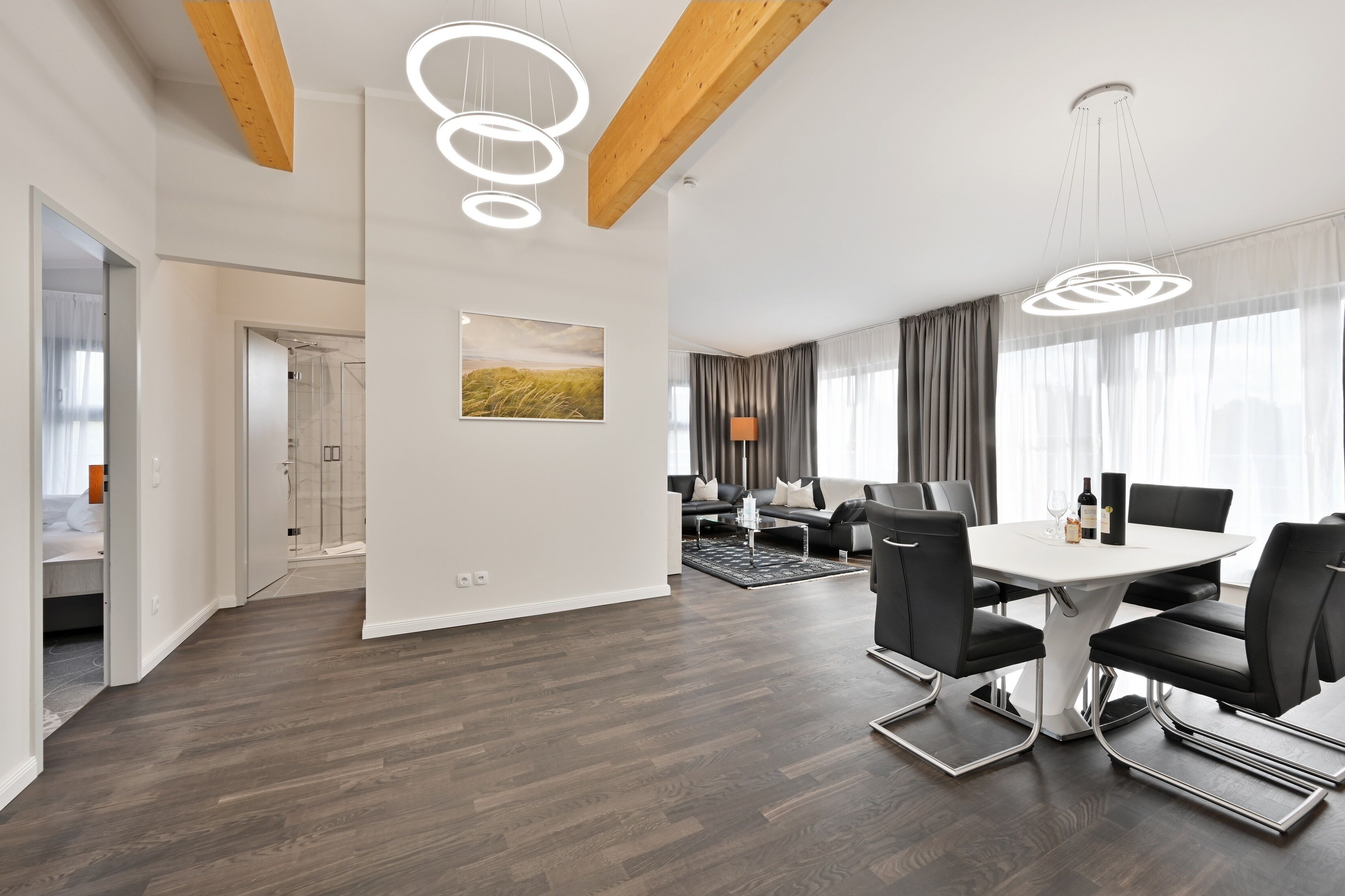 A modern hotel room with a wooden ceiling, a dining area with a round table and chairs, and a view of the outdoors through large windows.