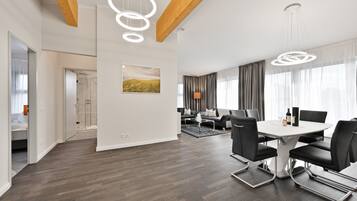 A modern hotel room with a wooden ceiling, a dining area with a round table and chairs, and a view of the outdoors through large windows.