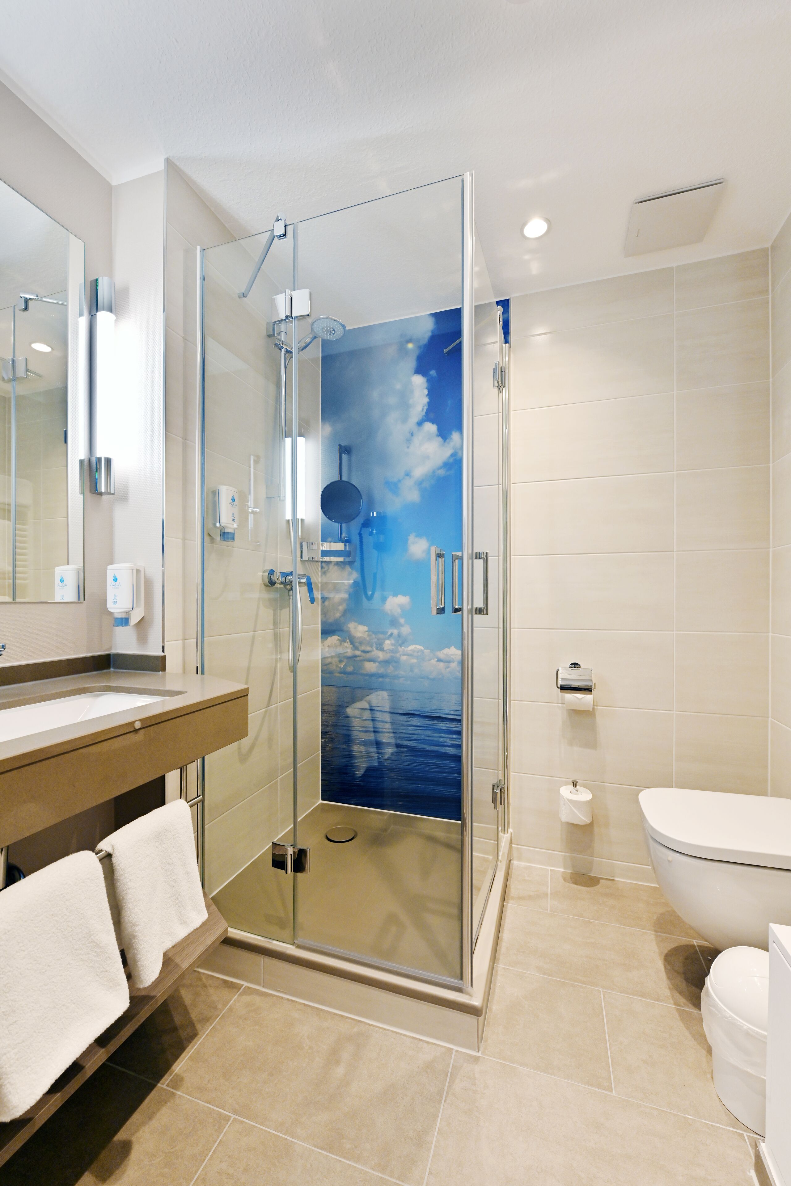 Une salle de bain moderne avec une douche à parois de verre, un grand miroir, un lavabo avec un meuble-vasque et des toilettes.