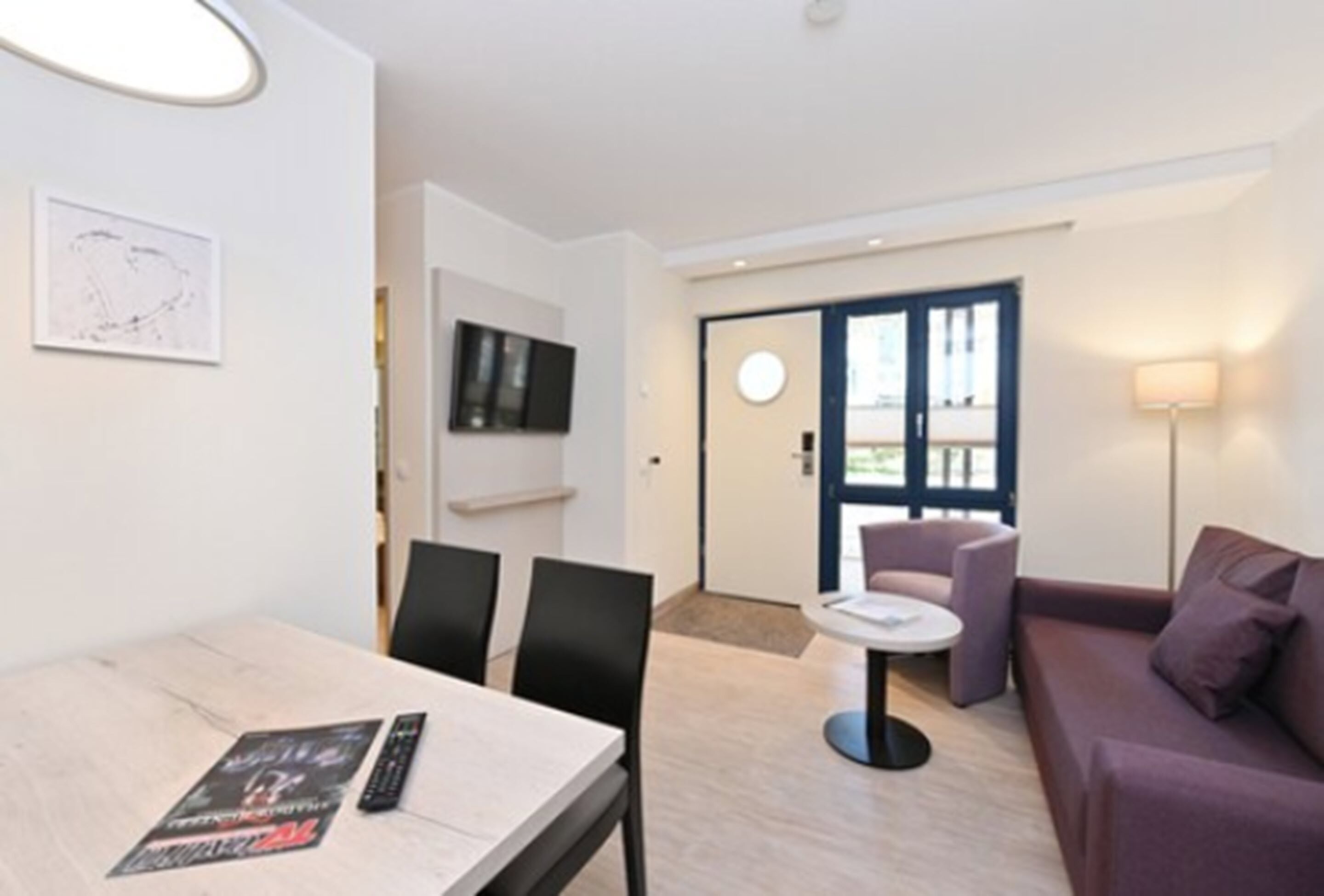 A modern hotel room with a dining area, a sofa, and a TV.